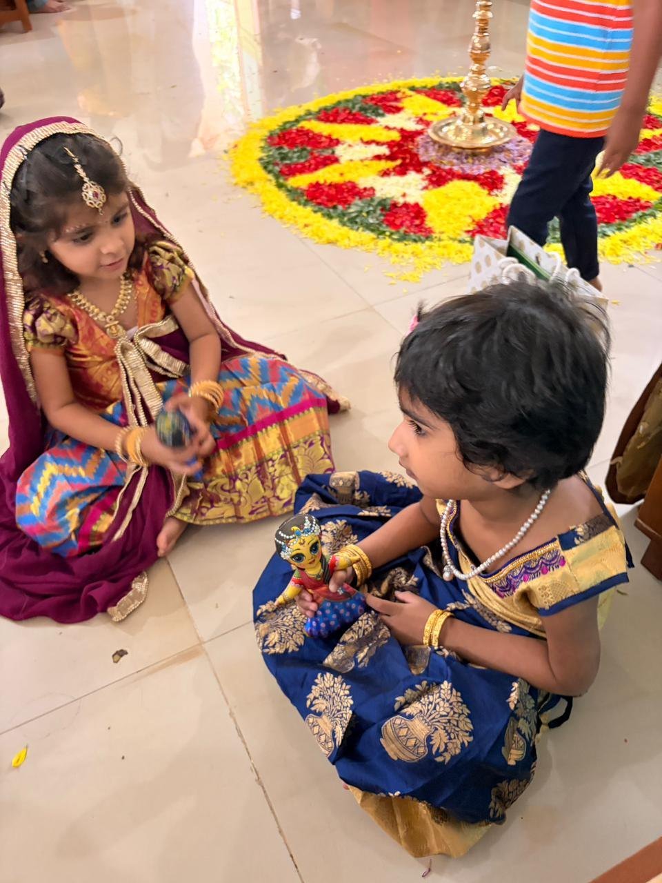Two children looking at their festival creations beside the Onam flower pookalam