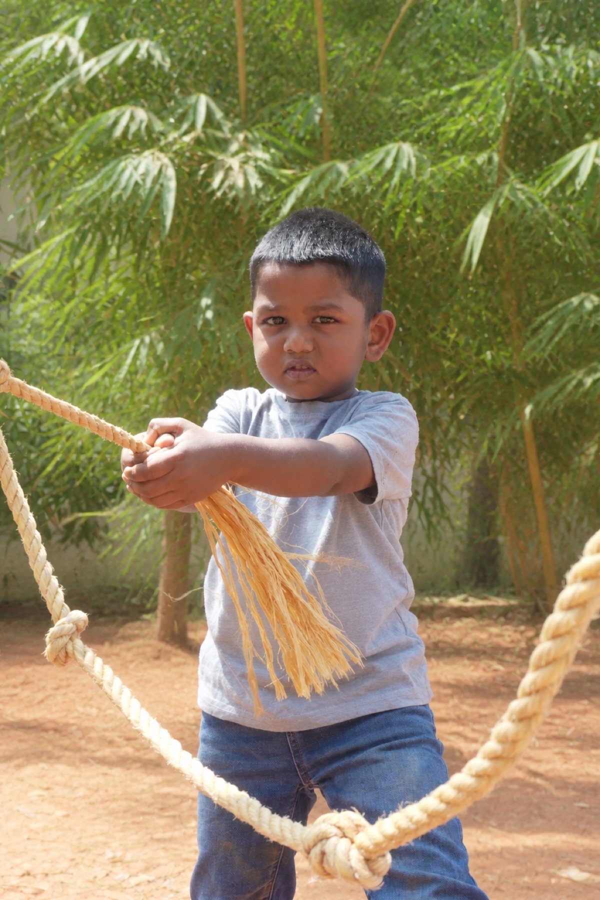 Arka child concentrating while holding a natural rope outdoors