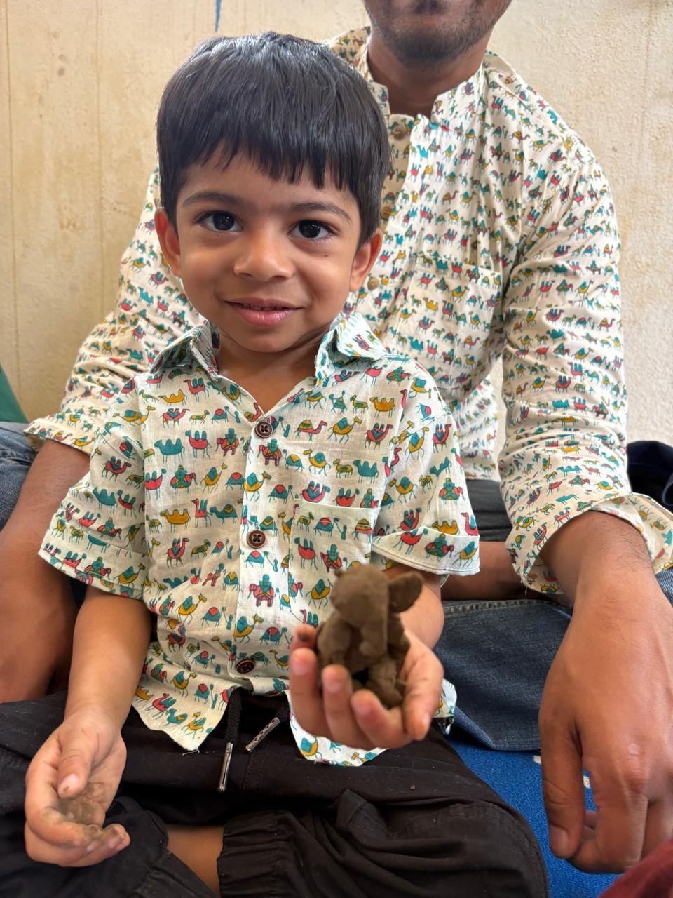 A child proudly showing his clay creation with a parent