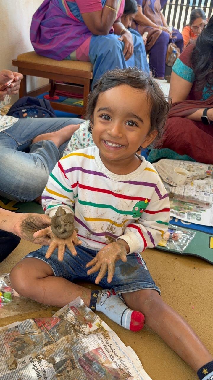 A smiling child showing a handmade clay Ganesha